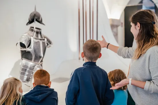 Museumsführerin zeigt Kindern eine Ritterrüstung im Ausstellungsraum